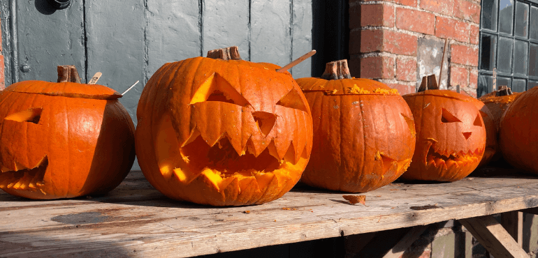 Orange coloured Pumpkins placed on a table which are crafted to look like human faces.