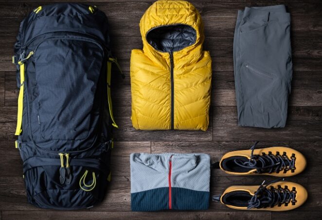 Hiking essentials placed on a table. A bag, jacket, shorts, t-shirt and shoes.