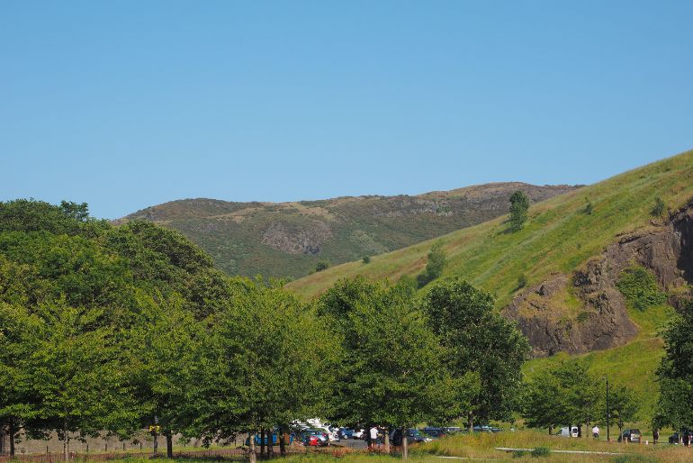 A lush green landscape with trees in the foreground and rolling hills in the background under a clear blue sky.