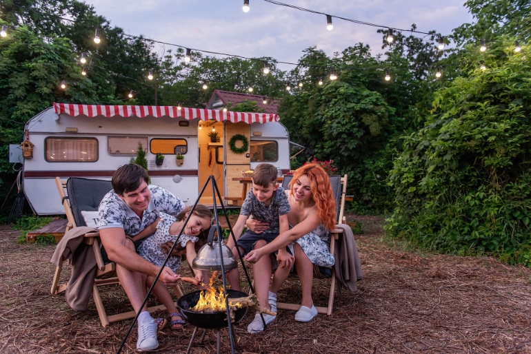 A family with two young children cooking on a campsite at dusk.