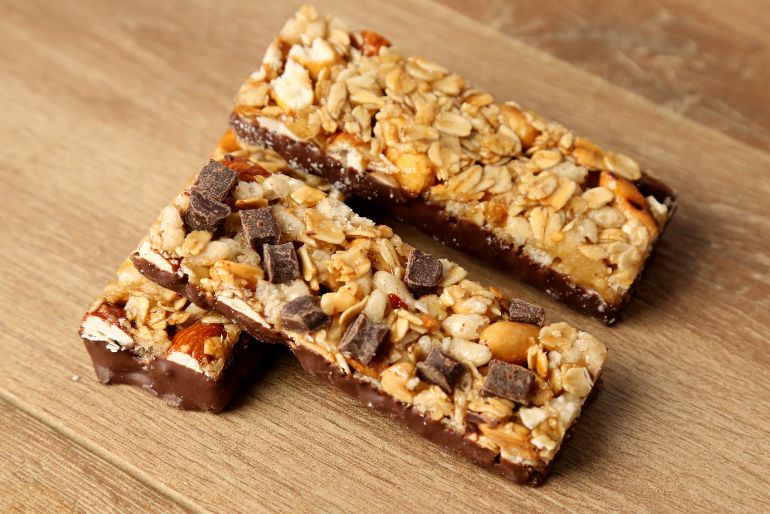 Two Nature Valley granola bars with oats, nuts, and chocolate chunks, resting on a wooden surface.