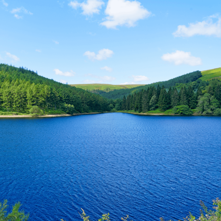 a serene reservoir with calm waters, surrounded by lush green mountains, reflecting the clear blue sky